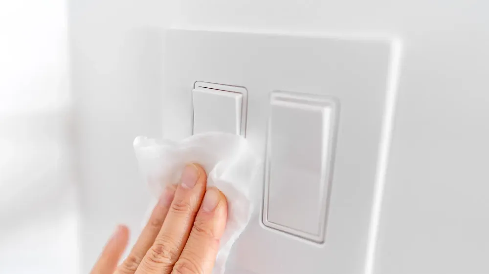 hands wiping lightswitch with disinfectant wipes